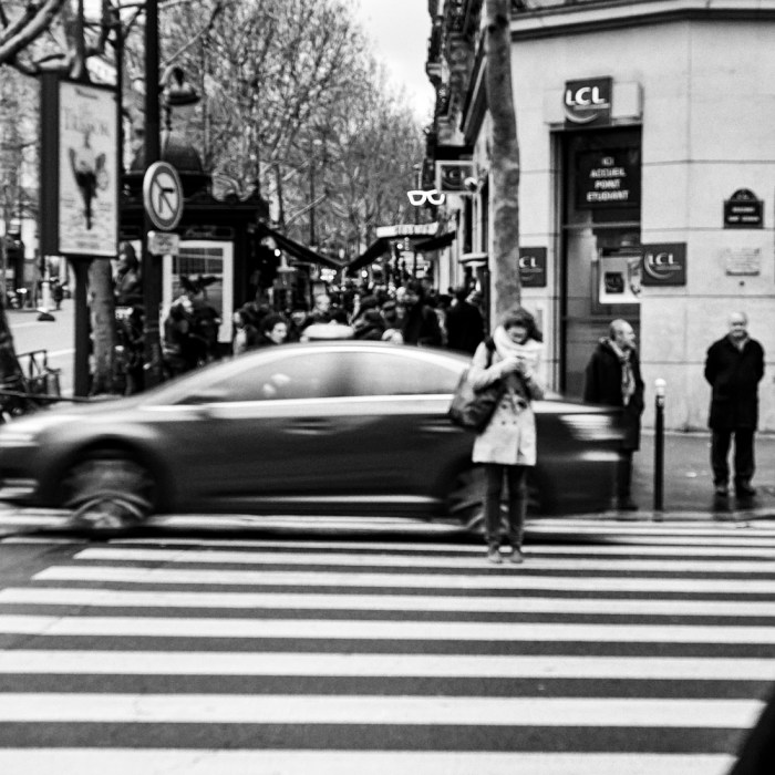 Moça destraída no celular parada no meio da rua em Paris.